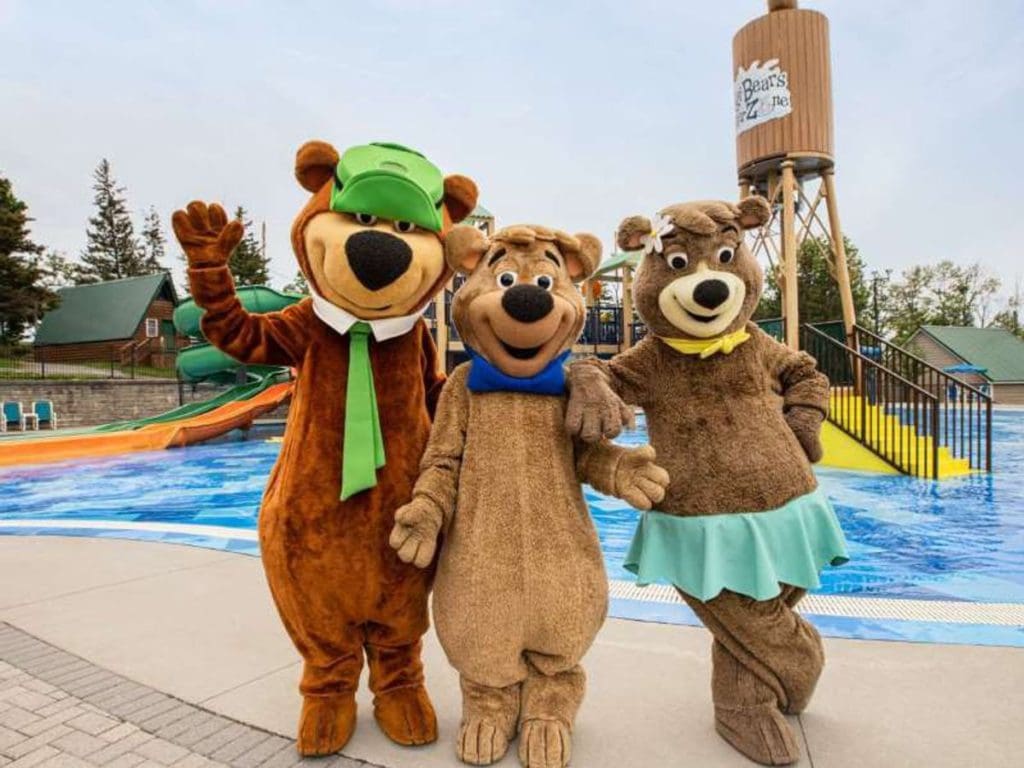Three Yogi Bear mascots stand in front of a water park at Jellystone Park in Western New York.
