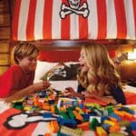 Two kids sit on a bed in a pirate-themed room looking at a large pile of legos.