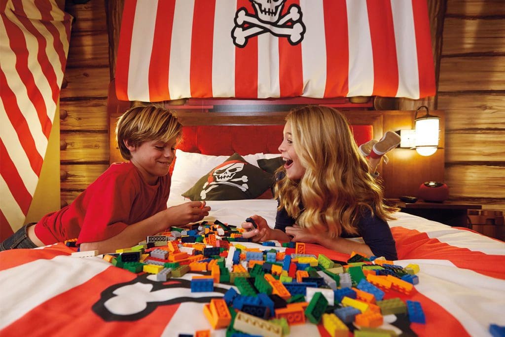 Two kids sit on a bed in a pirate-themed room looking at a large pile of legos at LEGOLAND Hotel, one of the best themed hotels in the United States for families.