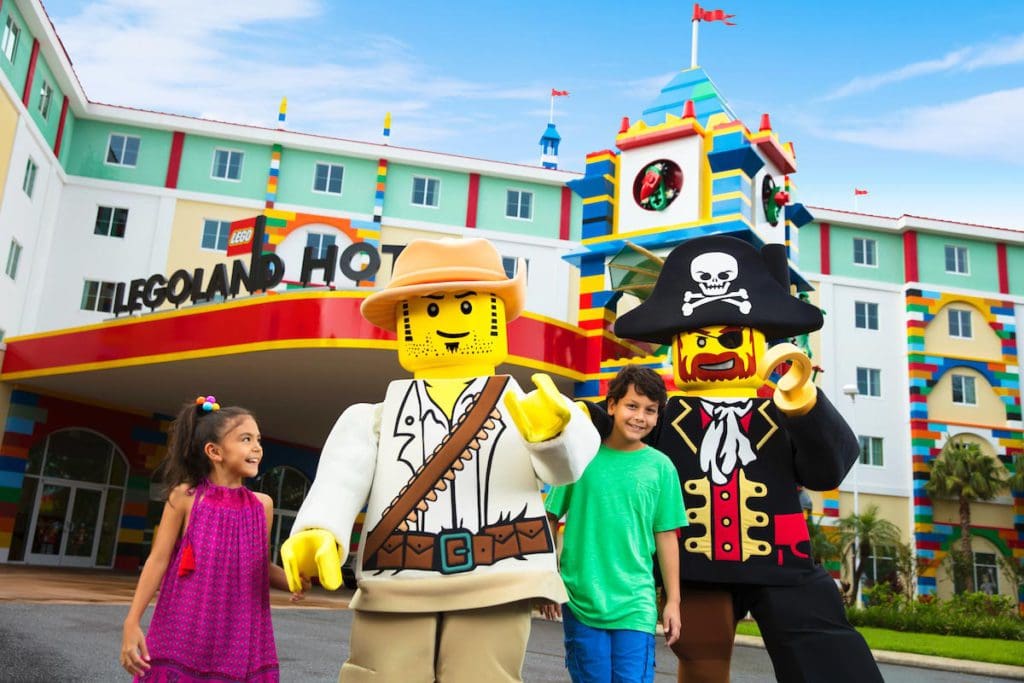 The exterior entrance to the LEGOLAND Hotel, featuring two lego-inspired mascots and two kids, one of the best themed hotels on the West Coast for families.