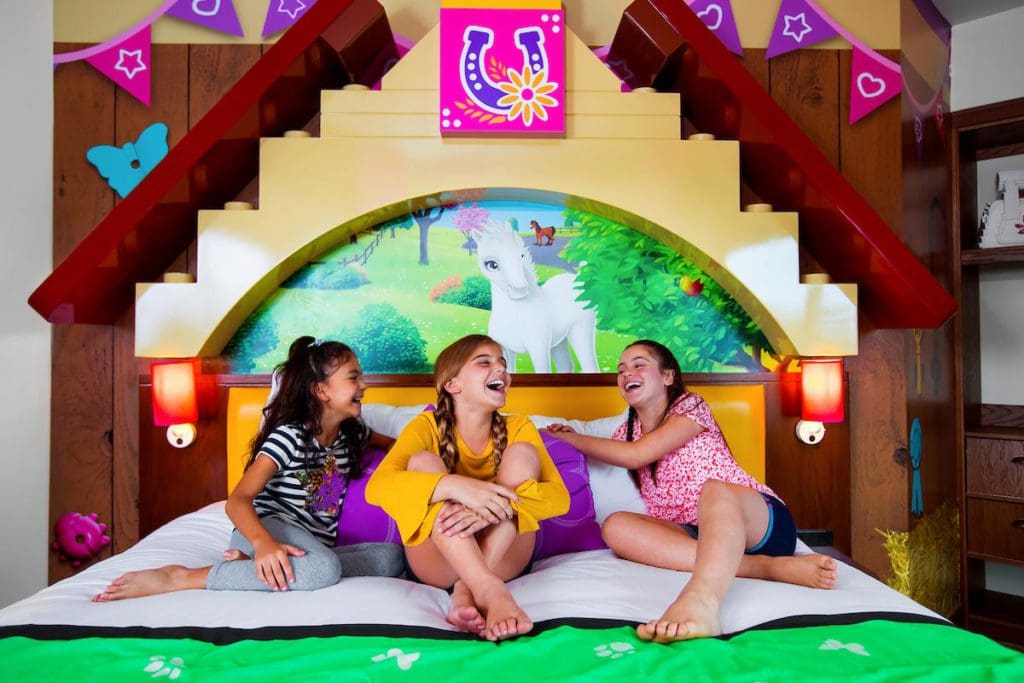Three teen girls sit on a LEGO Friends-themed bed at LEGOLAND Hotel.