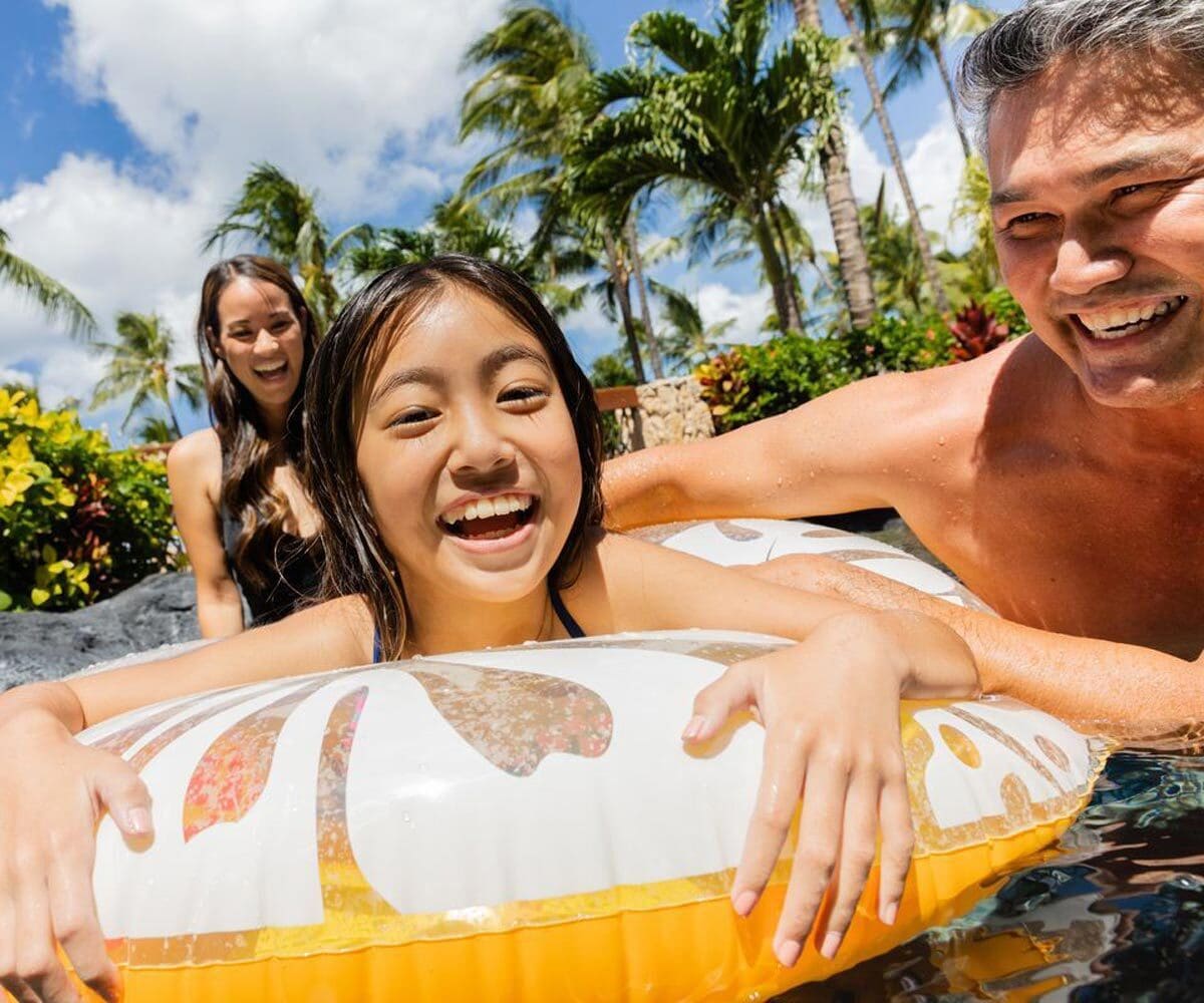 A dad holds onto his daughter, who floats in a yellow tube, while enjoy a sunny day on a lazy river.