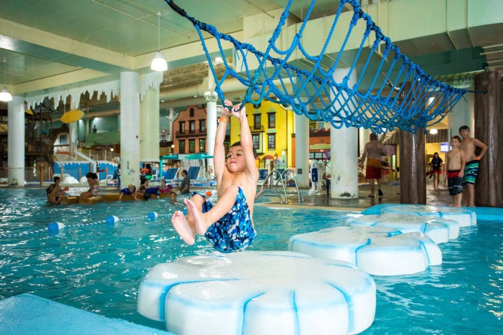 A young boy hangs on the ropes overhead as he crosses lily pads in the indoor water park at Boyne Mountain Resort.