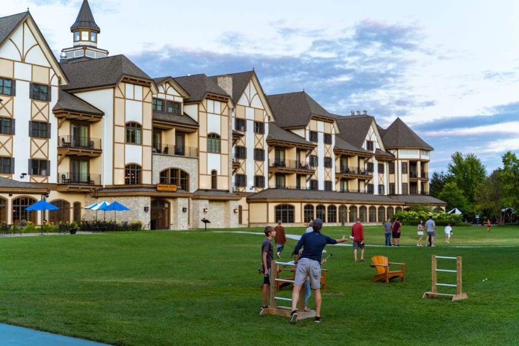 The exterior to Boyne Mountain Resort, with a lush green lawn in front, where families are playing outdoor lawn games.