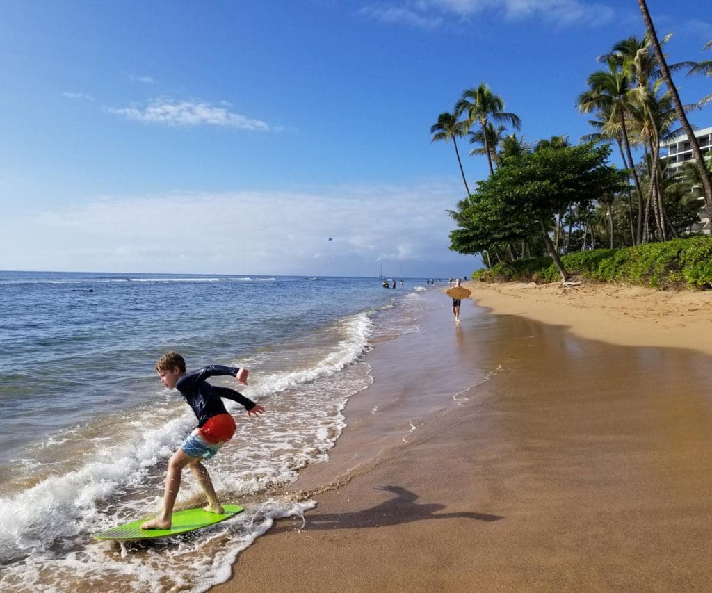 A young boy boogie boards along an oceanfront in Hawaii.
