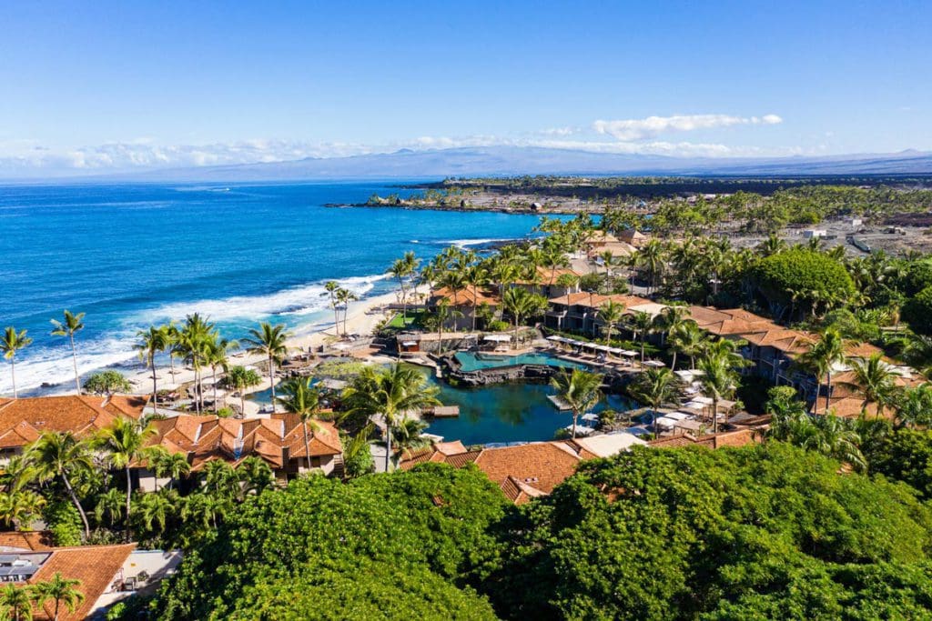 An aerial view of Four Seasons Resort Hualalai, featuring several resort buildings, lush greenery, and a view of the ocean, one of the best luxury hotels in the U.S for families.