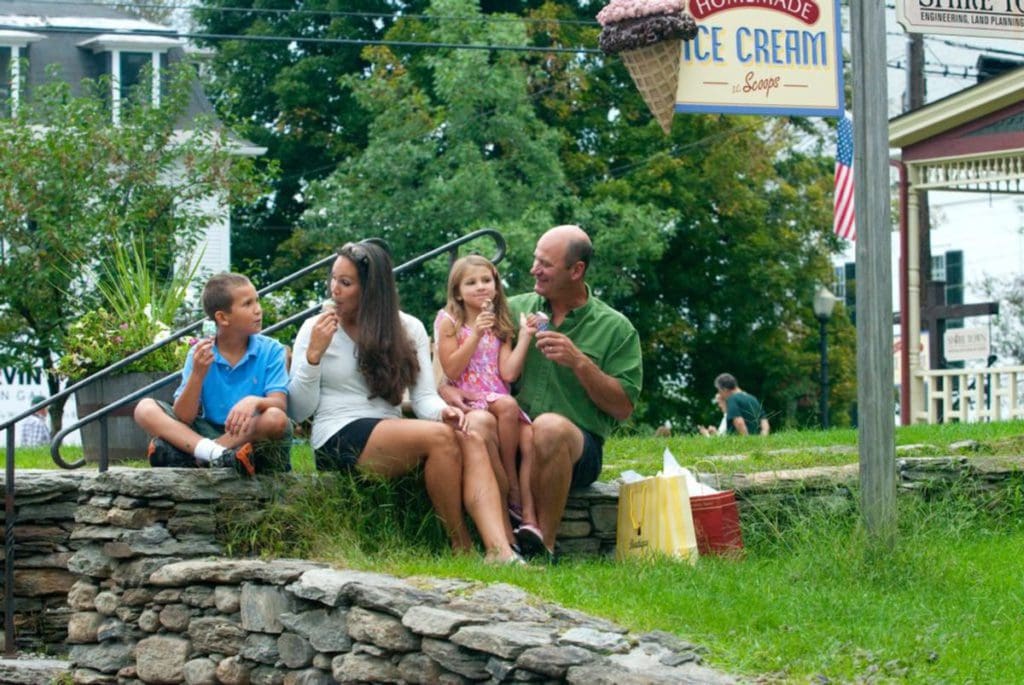 A family of four enjoys summer ice cream cones, while sitting along a sidewalk, in Stowe.