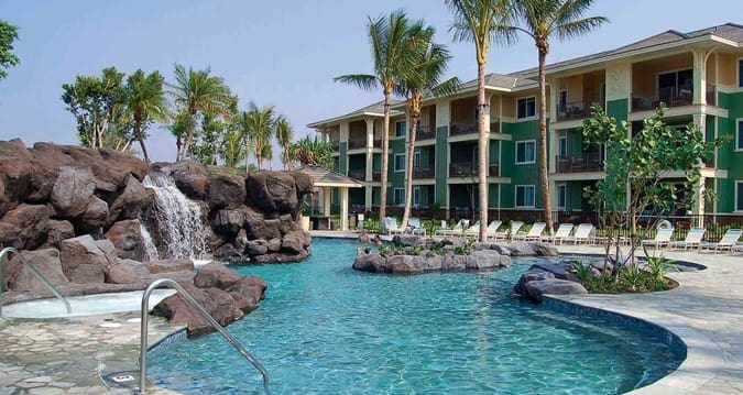 The pool, with a small waterfall going into it, and resort buildings in the distance at Hilton Grand Vacations Club Kings’ Land Waikoloa.
