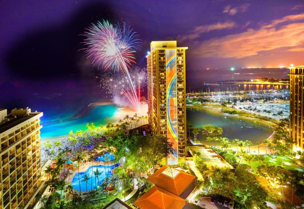 A stunning firework display over the grounds of Hilton Hawaiian Village Waikiki Beach Resort and nearby oceanfront at one of the best hotels in Hawaii for a family vacation.