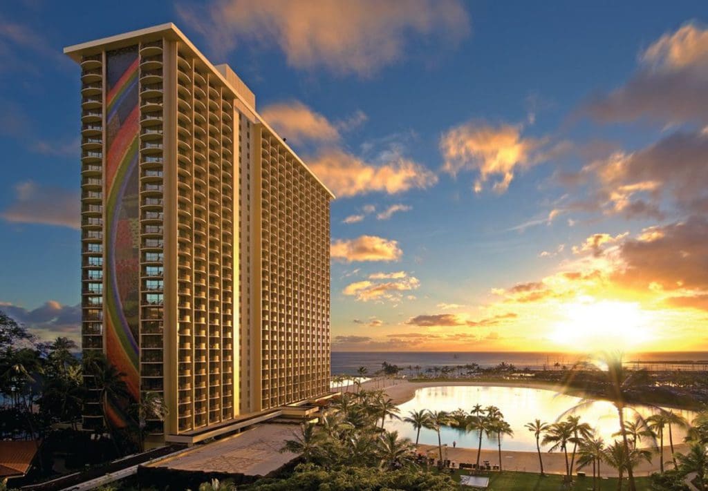 A view of the colorful Hilton Hawaiian Village Waikiki Beach Resort, with a view of the ocean and a gorgeous sunset in the distance at one of the best resorts for families in O'ahu.