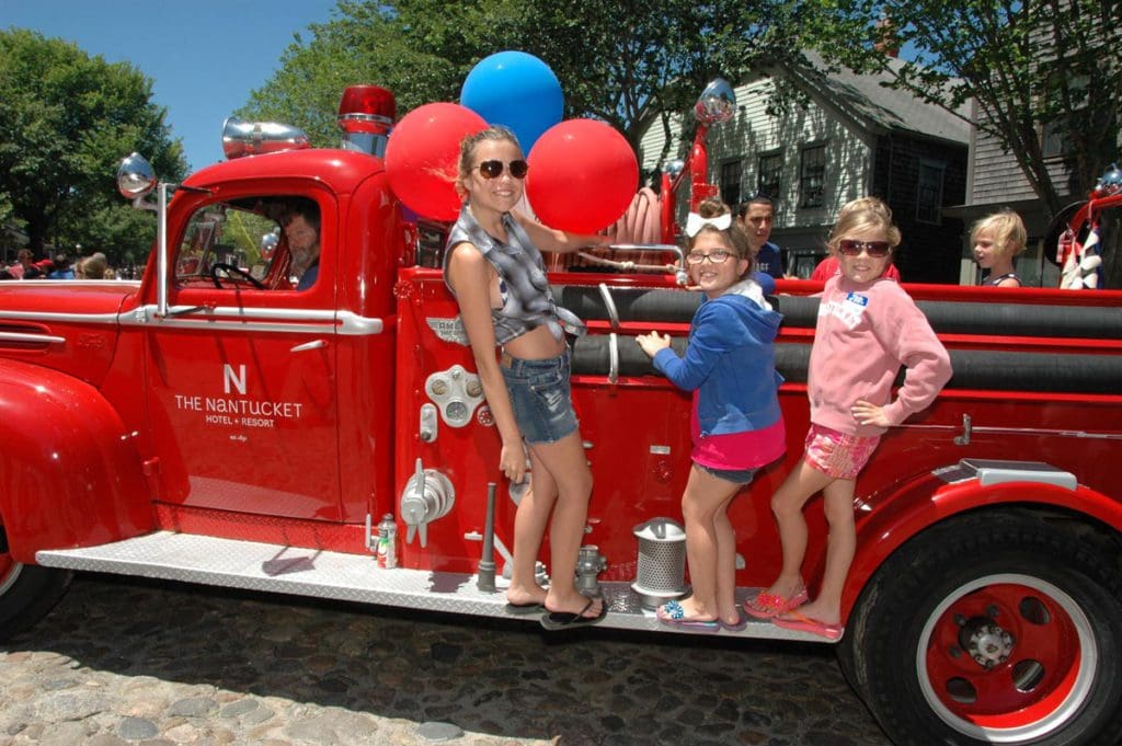 A mom and her two kids lean out from a firetruck with balloons during a Fourth of July parade in Nantucket.