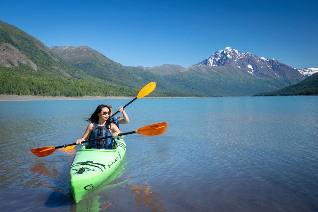 A mother and son tandem kayak along Eklutna, with mountains in the distance, near Anchorage. 
