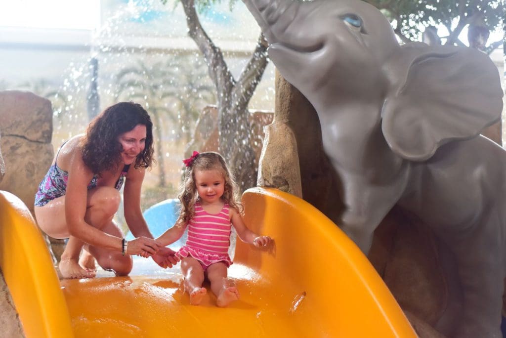 A mom helps her young daughter go down a small yellow slide at Kalahari Resort.