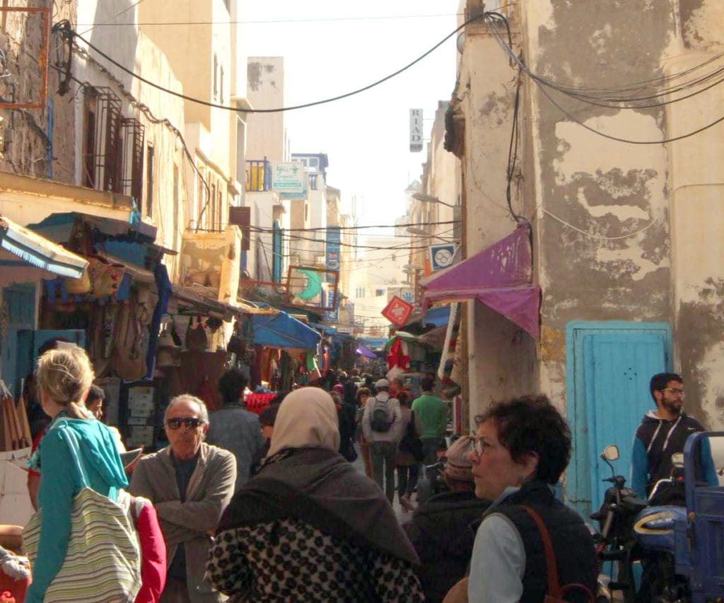 Crowds of people are meandering through a Moroccan street filled with vendors.