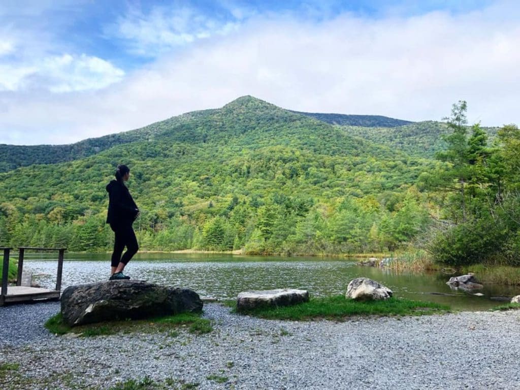 A teenagers stands on a large rock along the lake shore in Manchester, Vermont.