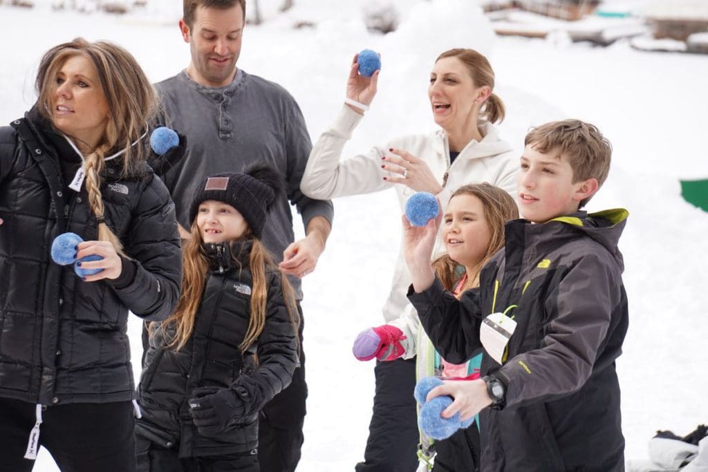 Several kids and an adult participate in a Winter Olympics game at Woodloch Resort by throwing blue balls at a target.