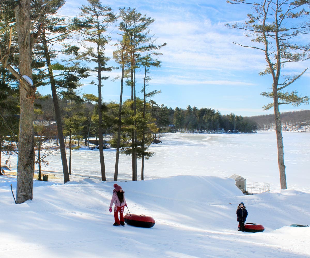 Two kids, pulling snow tubes, walk along a winter field at Woodloch Resort.