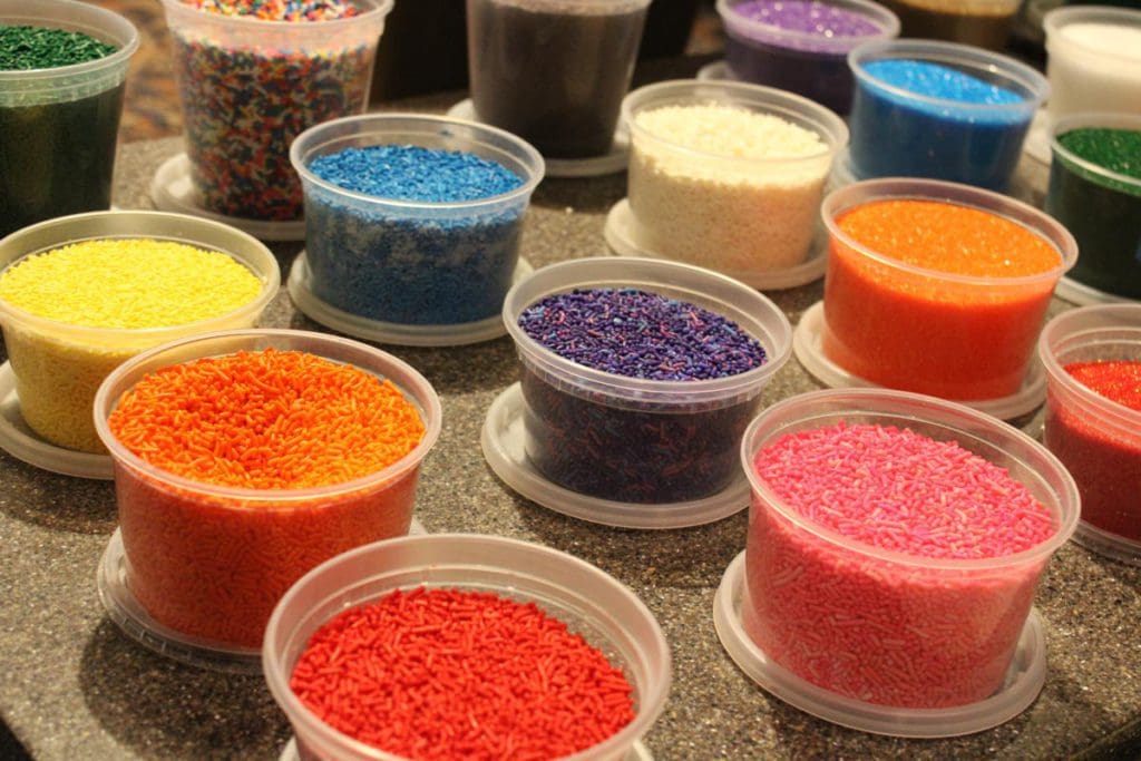 Several bowls of colorful sprinkles, including yellow, orange, red, pink, and purple.