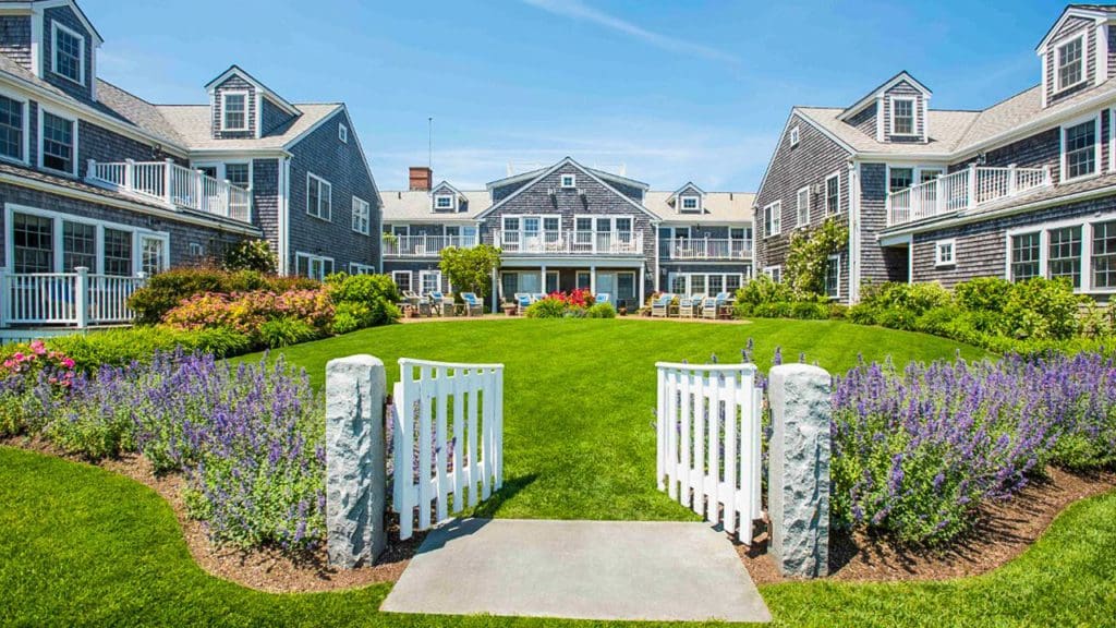 A white-picket fence, flanked by blooming flowers, leads to the entrance of White Elephant Nantucket.