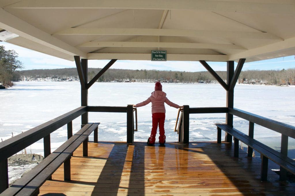 A young girl stands at the end of a dock at Woodloch Resort, looking out onto the frozen lake.