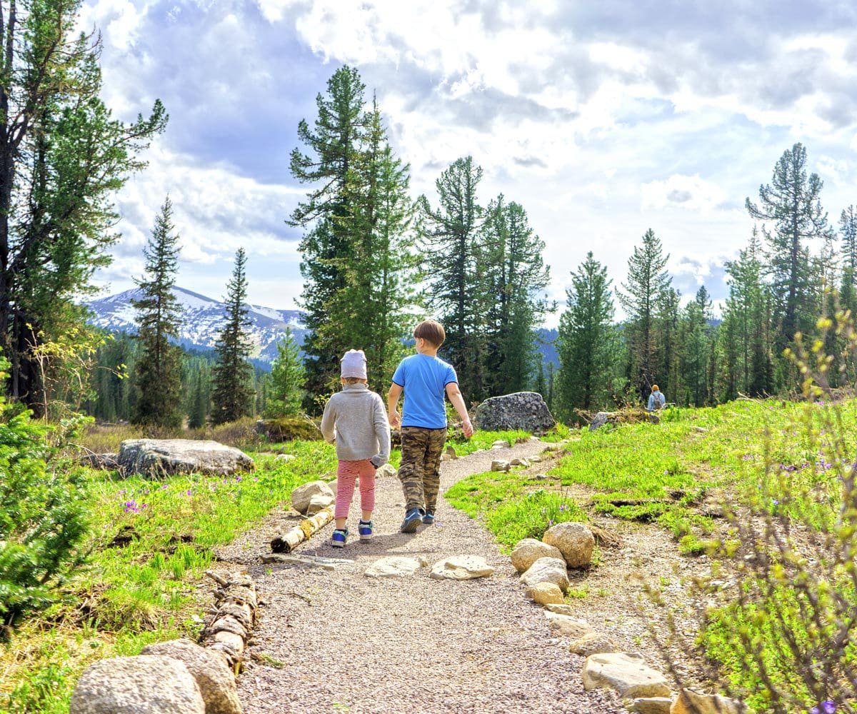 Two small kids walk together along a hiking path in Colorado.