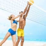 A man and woman, both in swimsuits, meet at a volleyball net on the beach to push the ball over the net at Finest Playa Mujeres in Cancun.