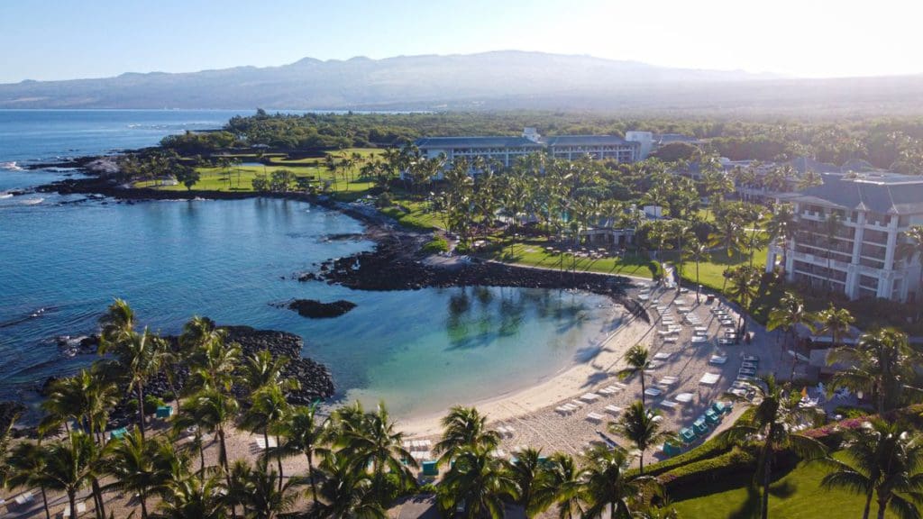 An aerial view of the bay and ocean shores of Fairmont Orchid, Hawaii, with resort buildings set around the property.