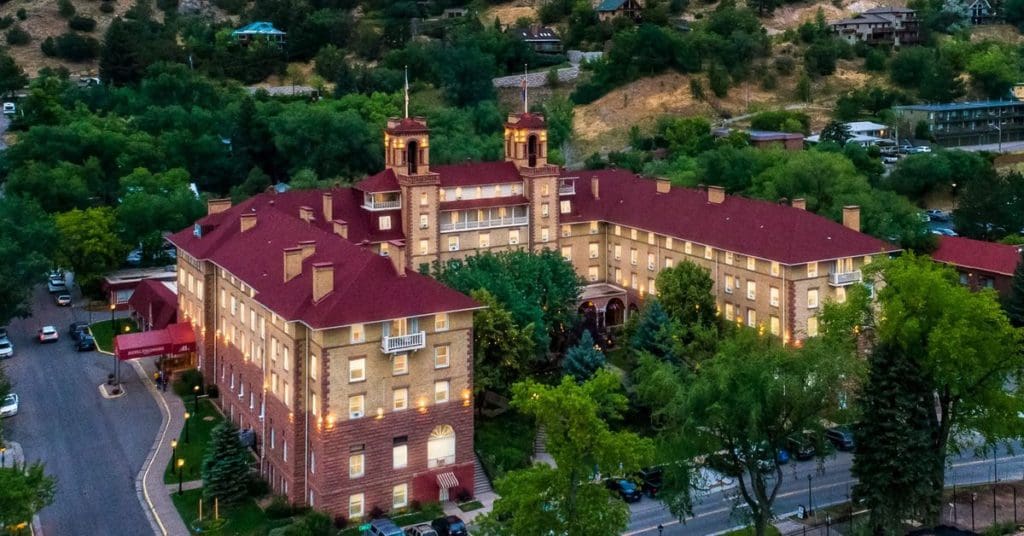 An aerial view of Hotel Colorado in Glenwood Springs, featuring its iconic red roof and historic features amongst lush summer trees.