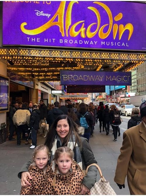 A mom and her two young daughters stand outside the Broadway show Aladdin.