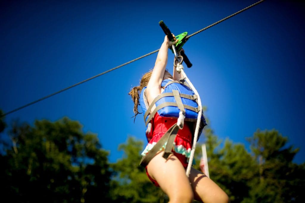 A young girl wearing a life jacket zooms along a zipline at Ludlow’s Island Resort.