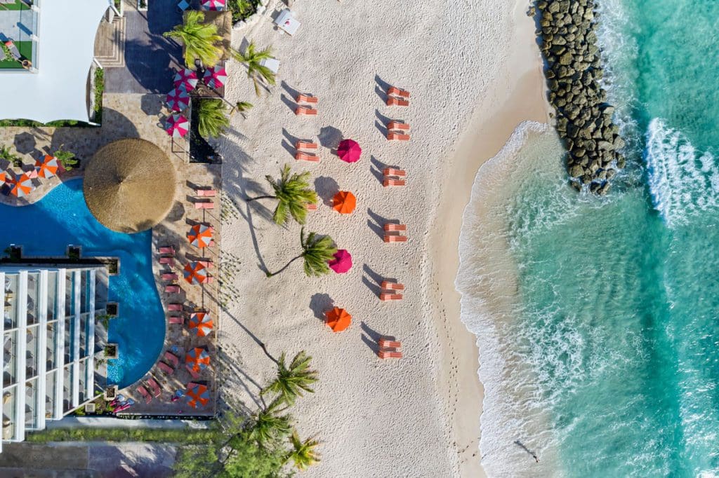 An aerial view of several colorful beach umbrellas near the ocean shore of O2 Beach Club and Spa, with resort buildings behind them.
