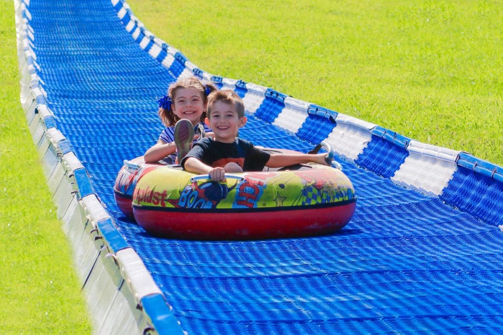 Two kids ride a tandem tube down an outdoor slide at Rocking Horse Ranch.