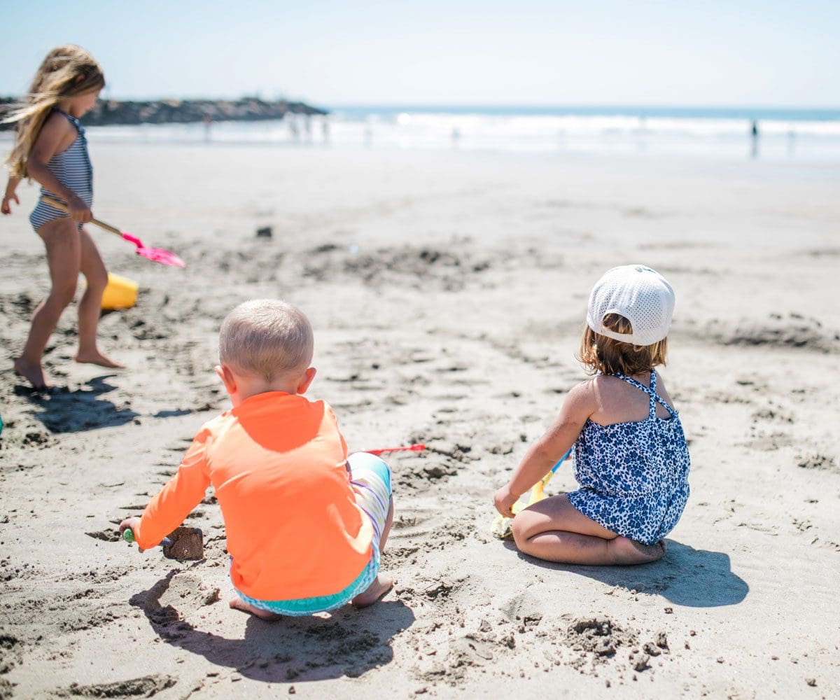 Three kids play on a beach near San Diego, with their own sand toys.