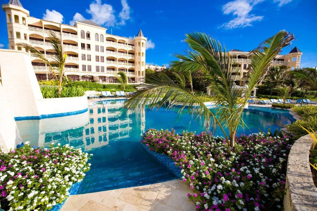 The pristine pool, surrounded by lush foliage, and resort buildings in the background of The Crane Resort, Barbados.