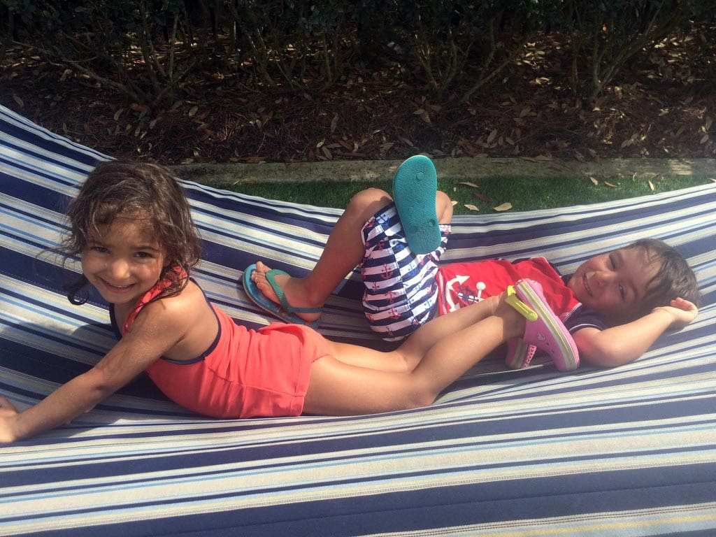 Two kids snuggle together on a hammock, while staying at a Waldorf Astoria property.