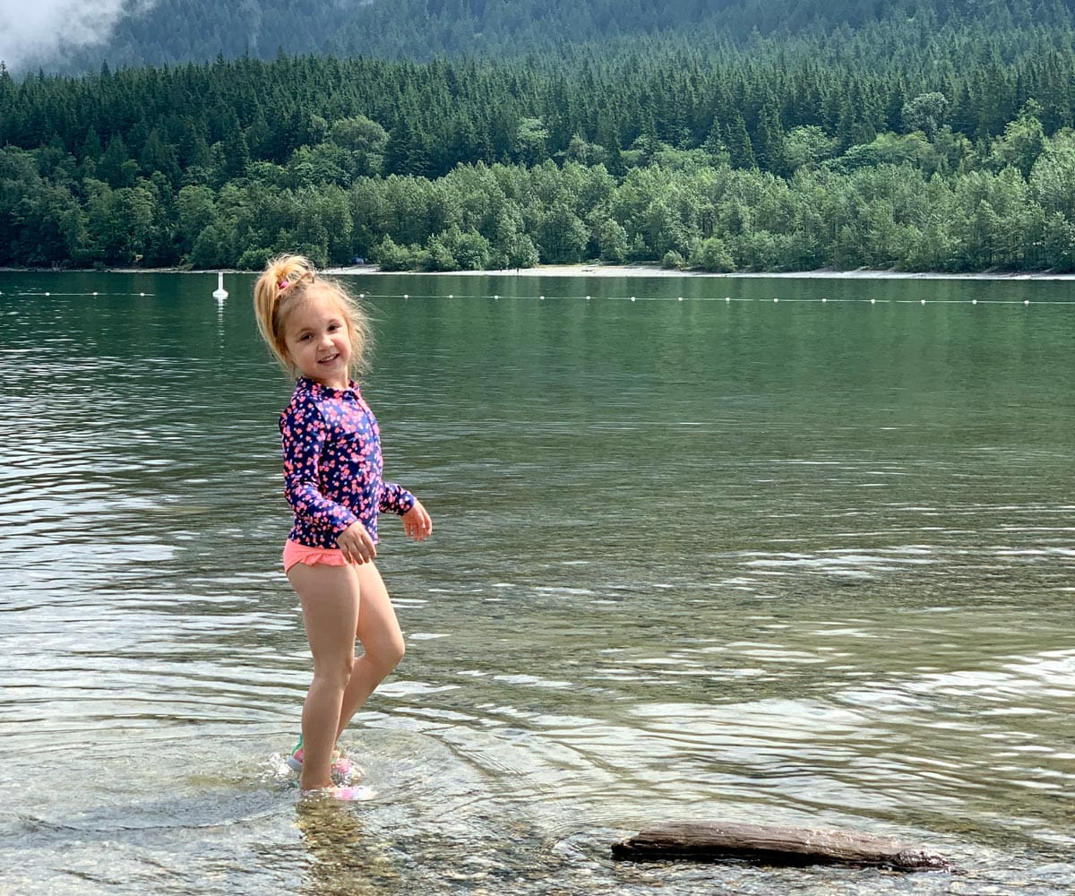 A young girl wearing a swimming suit stands on the shores of the lake within Golden Ears Provincial Park in British Colombia,
