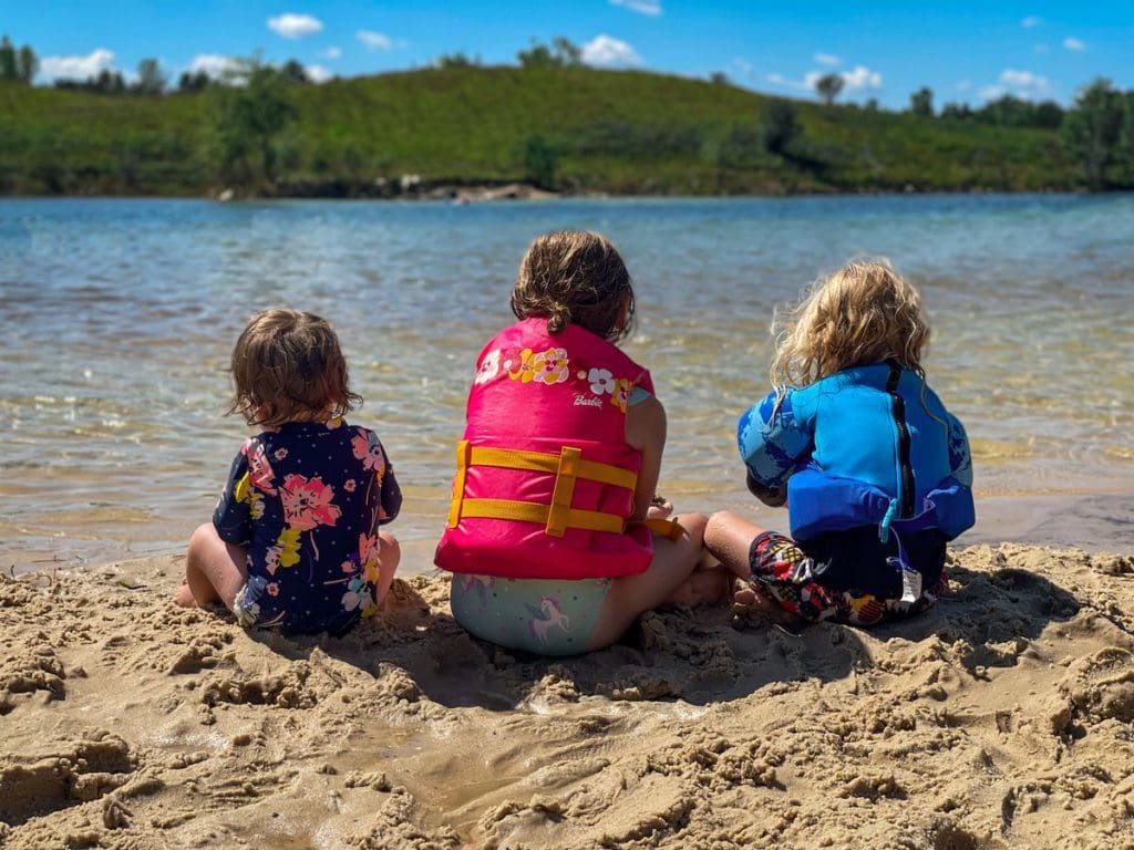 Three kids in swim suits and life jackets sit at the edge of Lake Wazee, one of the best places to visit in Wisconsin for families.