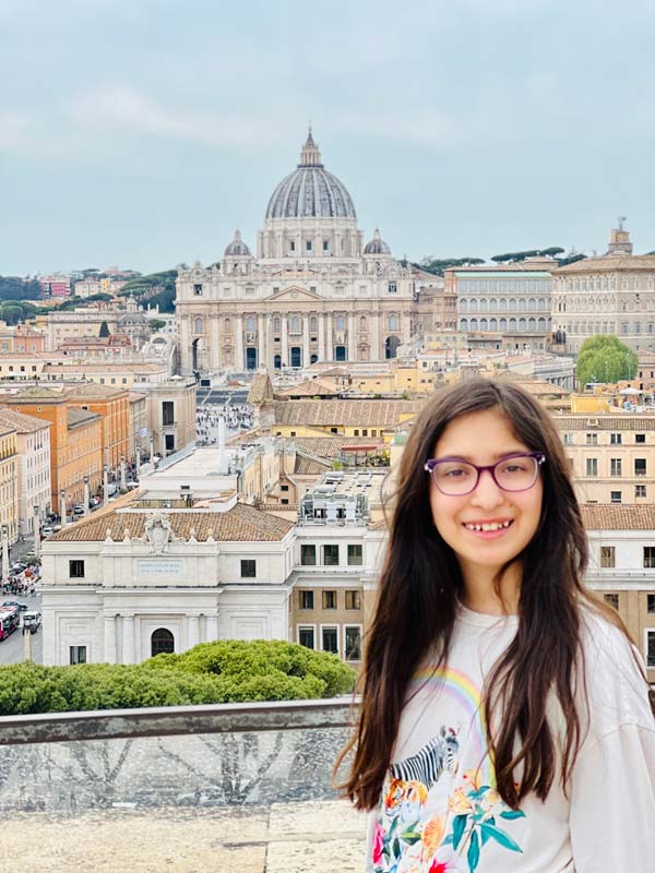 A young girl stands at the top of Castel Sant'Angelo, with a view of St. Peter's Basilica in the distance.