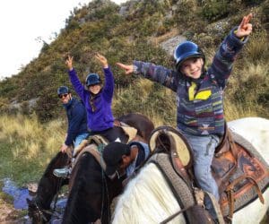 Two kids raise their hands in glee, while exploring Peru on horseback.