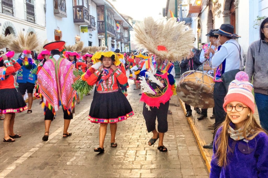 A young girl enjoys a vibrant parade of dancers on a street in Cusco.