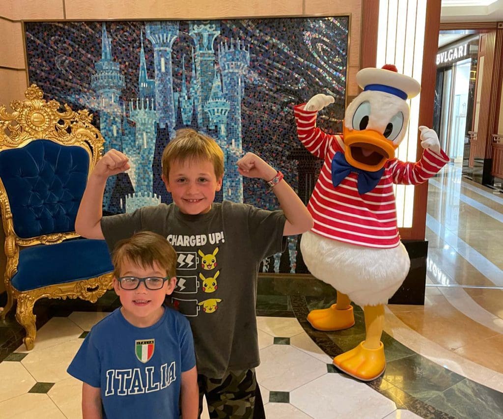 Two young boys pose excitedly with Donald Duck on a Disney Cruise ship.