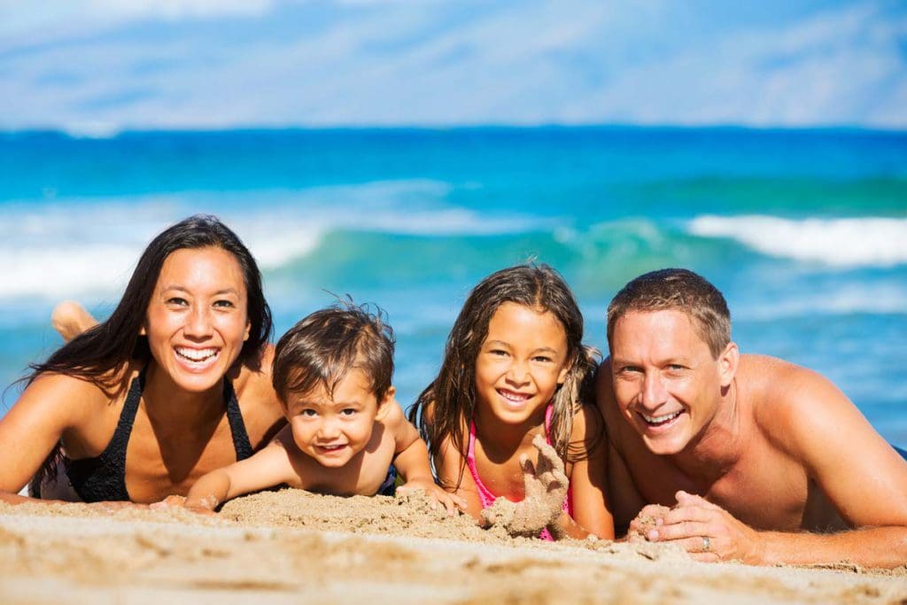 A family of four lays on the beach together smiling brightly during a family photo shoot, one of the best things to do in Oahu with kids.