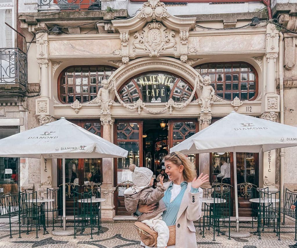A mom and her young daughter laugh, while standing in front of Majestic Cafe, a must stop on our 1-Week Porto itinerary with toddlers.