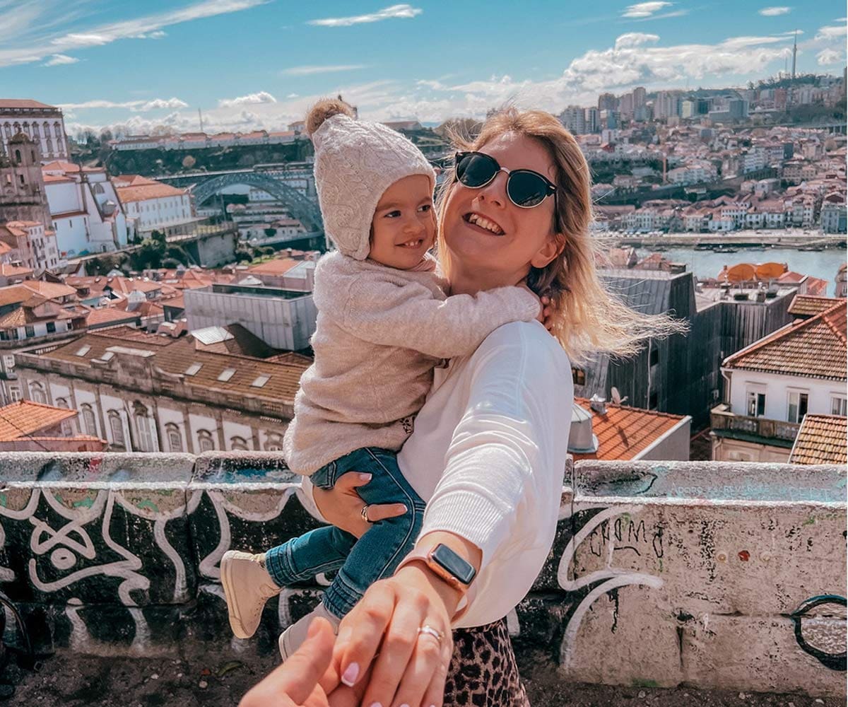 A mom holds her toddler, with a view of Porto in the distance.