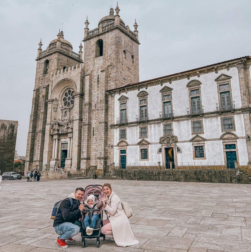 A family of three, with the toddler in a stroller, stand in front of Se Cathedral in Porto.