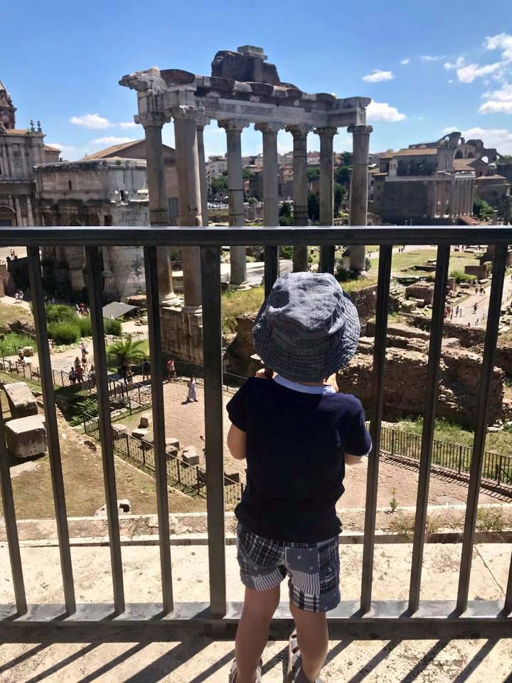 A young boy looks through a fence at ancient ruins inside the Roman Forum.