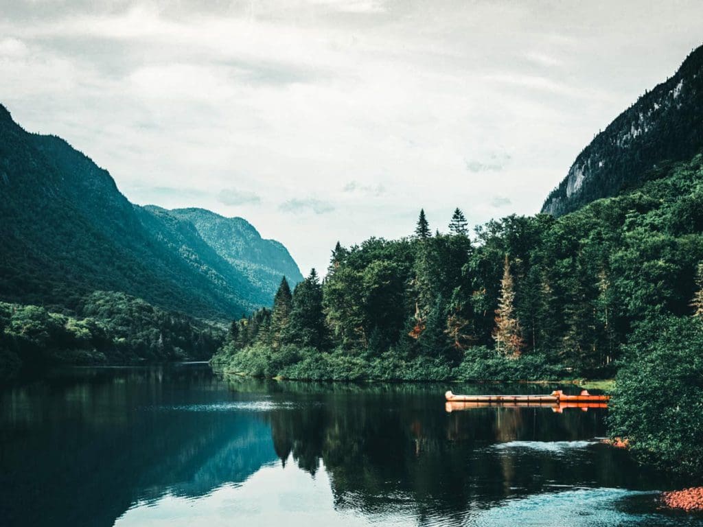 A canoe rests along a dock near a large lake flanked by giant pine trees at Jacques Cartier National Park.