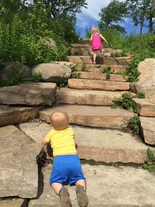 A young girl walks, and a baby boy crawls, up stone stairs in Madison's Picnic Point.