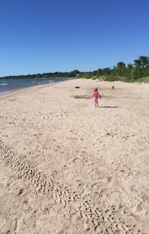 A toddler girl runs across a beach in Sheboygan, Wisconsin, on a sunny day.