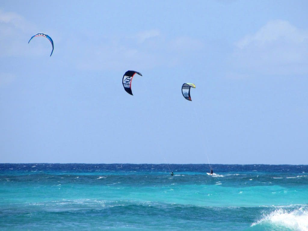 Three kite surfers jump high waves in Barbados.